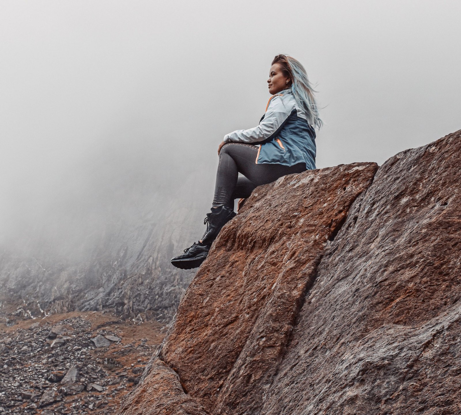 A woman sits on the edge of a rock in the misty mountains of Wales, UK, capturing adventure and solitude.